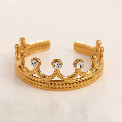 Gold crown-shaped ring with embedded crystals on a light beige background