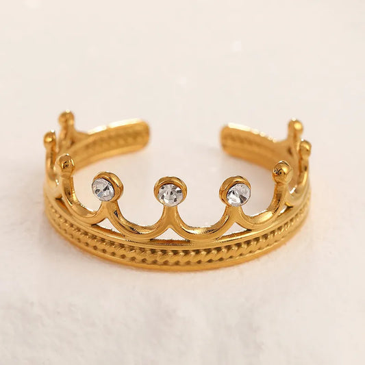 Gold crown-shaped ring with embedded crystals on a light beige background