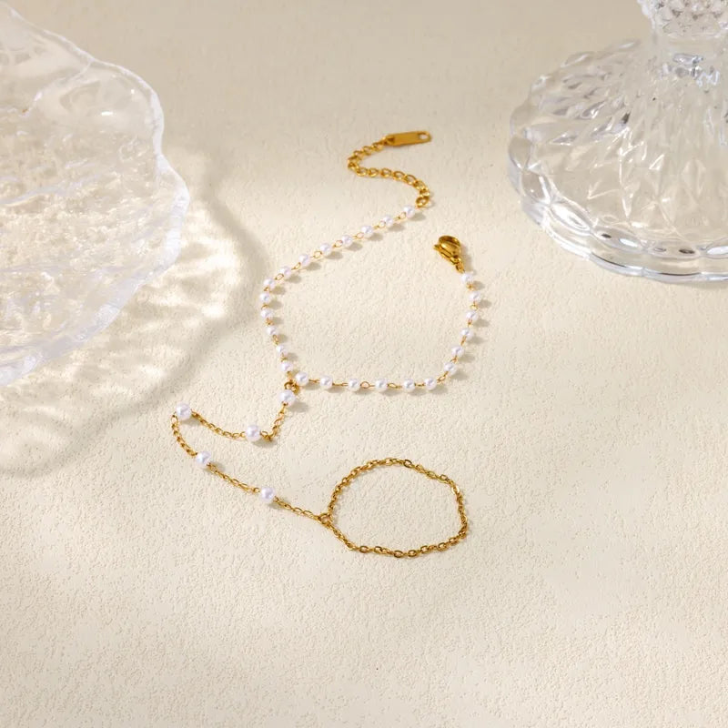 Gold necklace and bracelet set on a beige surface with a glass object in the background