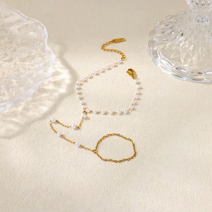 Gold necklace and bracelet set on a beige surface with a glass object in the background