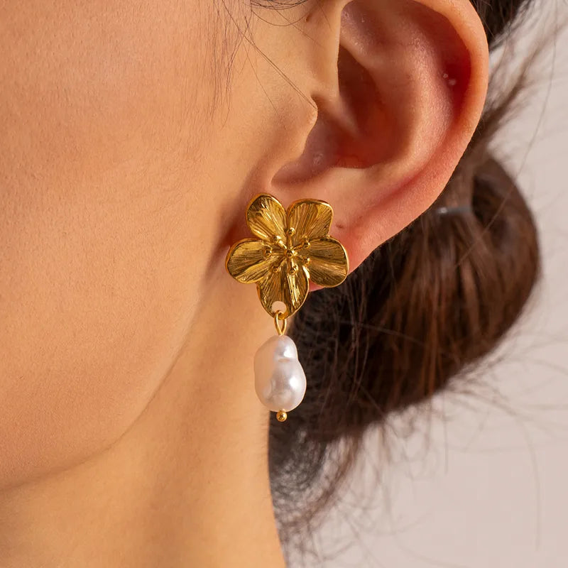 Gold flower earring with a pearl drop worn by a person.
