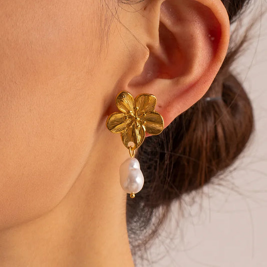 Gold flower earring with a pearl drop worn by a person.