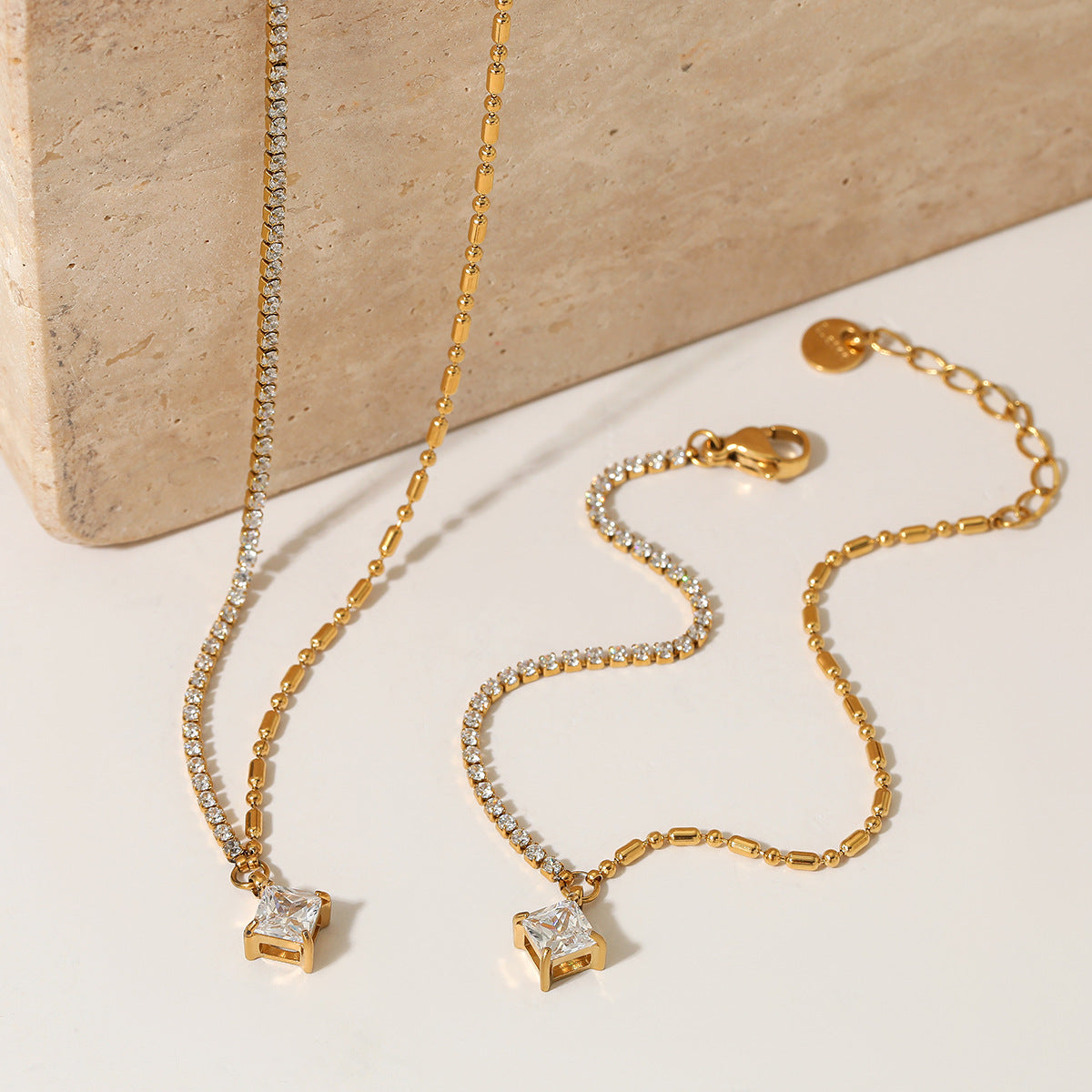 Gold necklace with diamond pendants on a beige stone surface