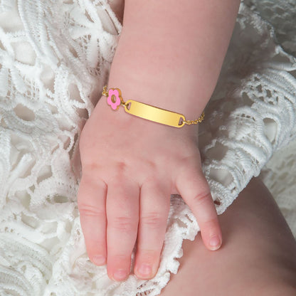 Gold baby bracelet with a pink flower charm on a child's wrist against a white lace background