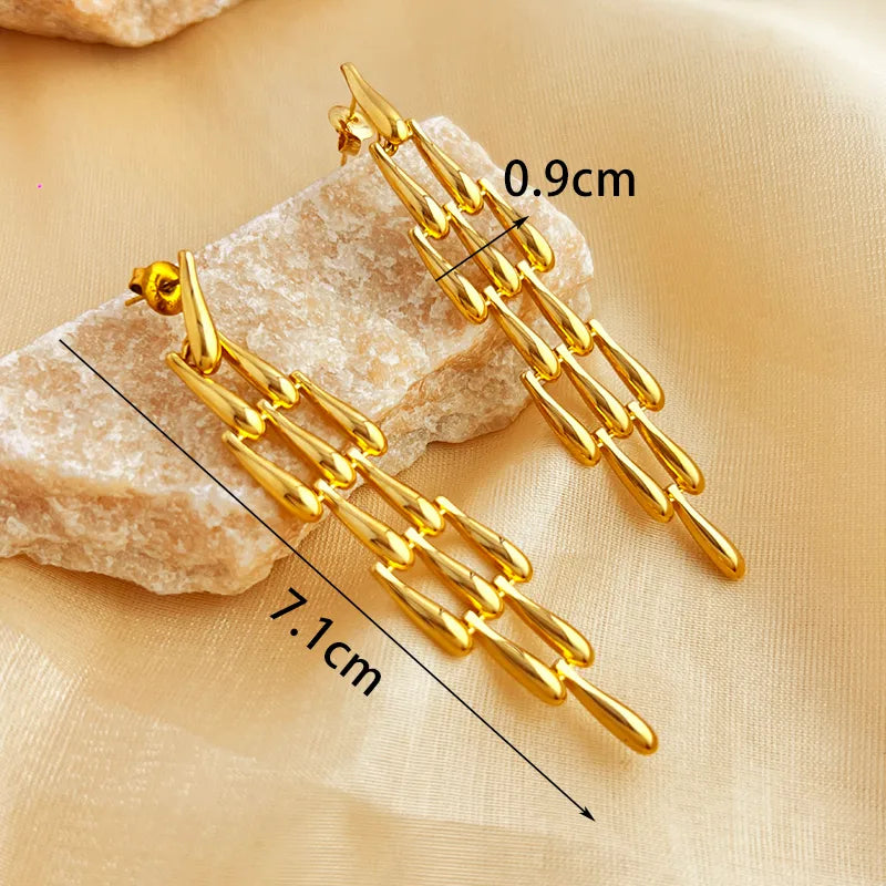 Gold earrings with measurements on a beige fabric background
