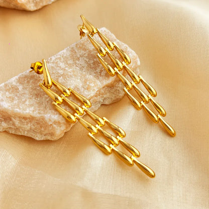 Gold chain earrings on a beige stone surface