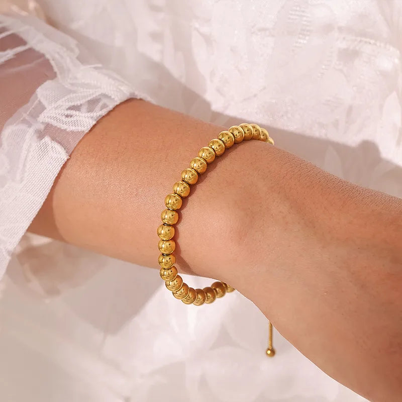 Gold beaded bracelet on a wrist with a white lace garment in the background