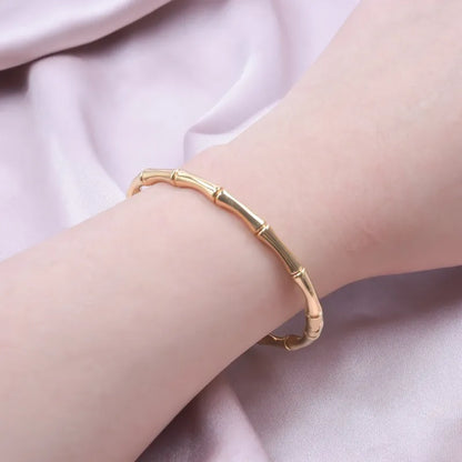 Gold bracelet on a person's wrist with a soft pink fabric background