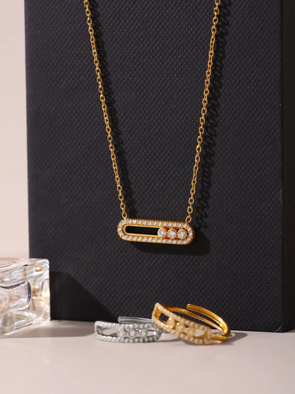 Gold necklace with diamond accents on a black textured background, with three additional gold rings in the foreground.