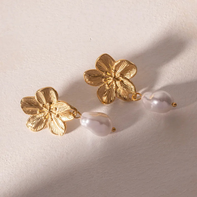 Gold floral earrings with pearls on a light beige background