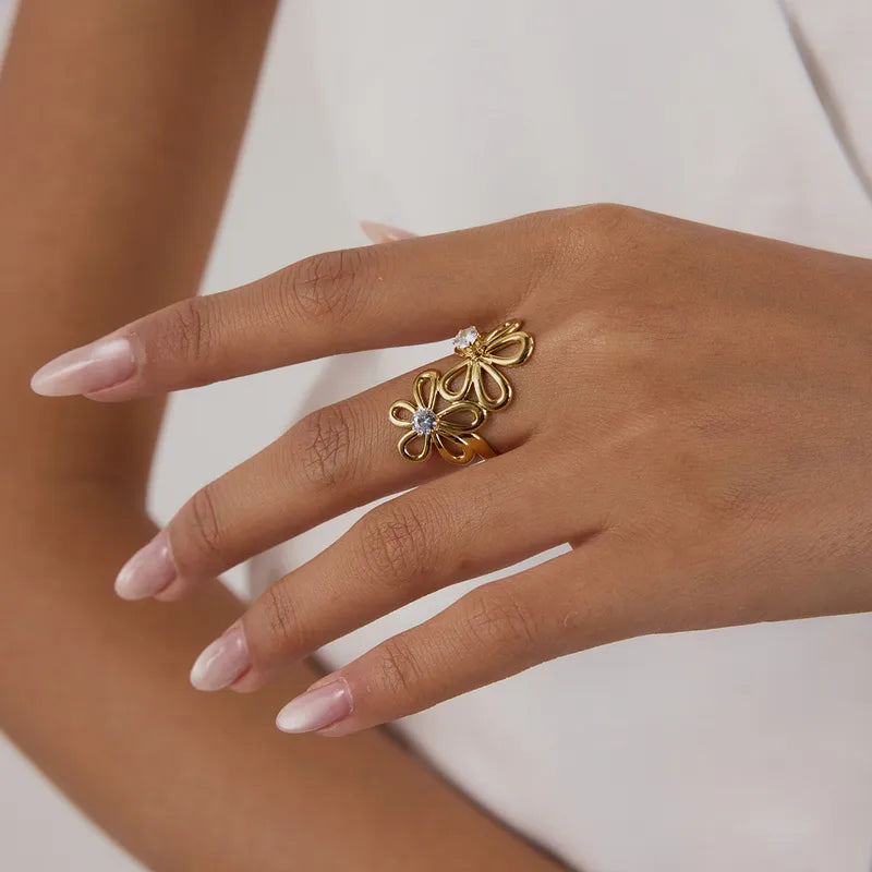 Gold floral ring on a person's finger with a plain background
