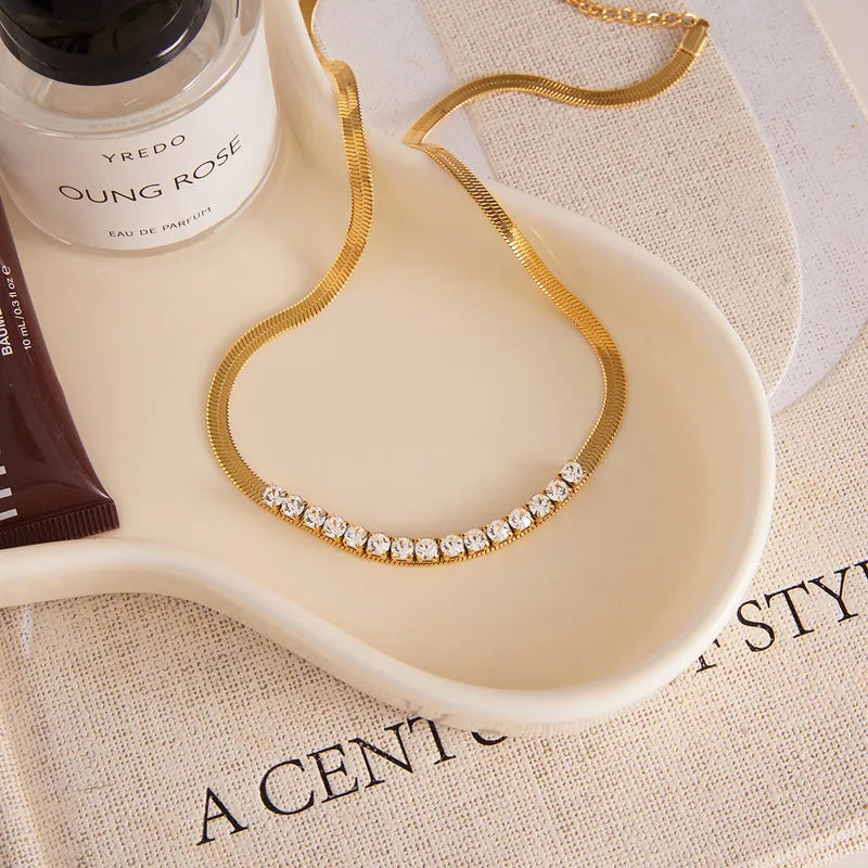 Gold necklace with crystals on a white dish, next to Yves Rocher and Yves Saint Laurent products on a magazine.
