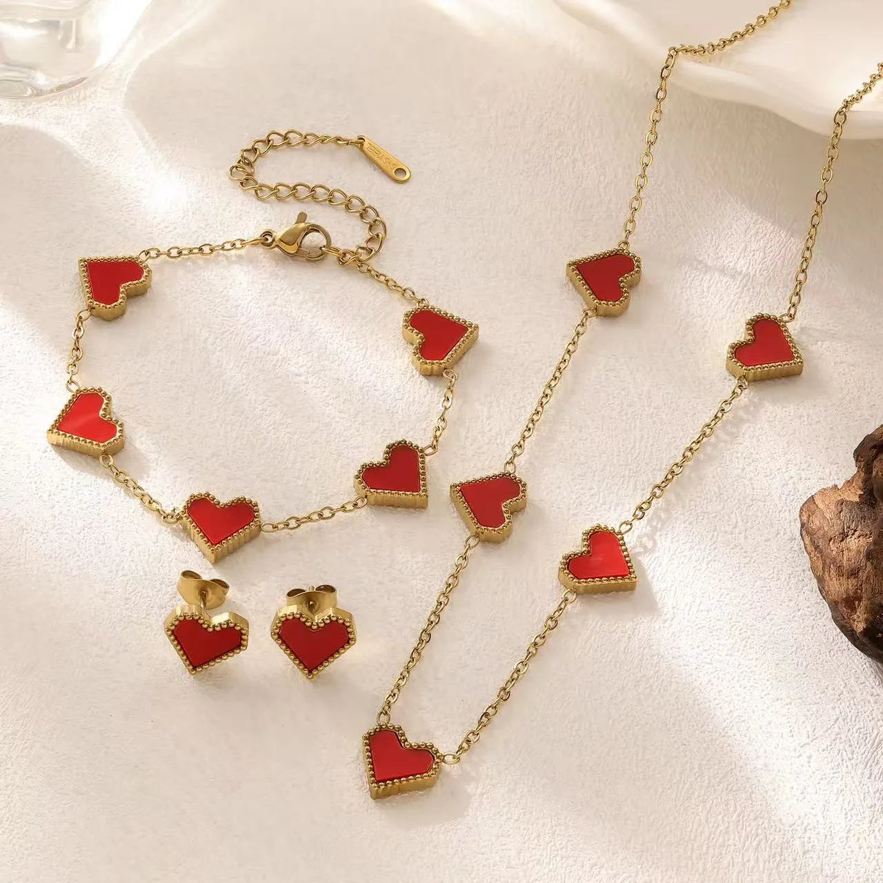 Gold necklace with red heart pendants on a white surface