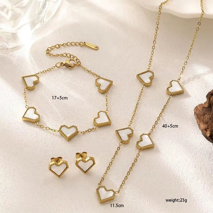 Gold heart-shaped jewelry set including necklace, bracelet, and earrings on a light background.