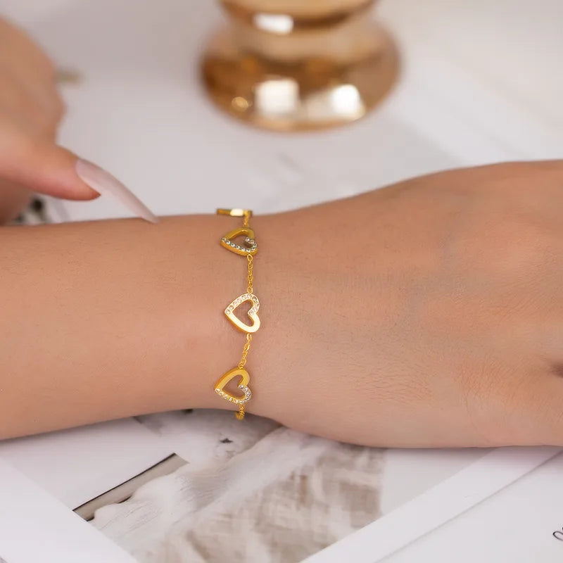Gold bracelet with heart-shaped links on a wrist, with a blurred background