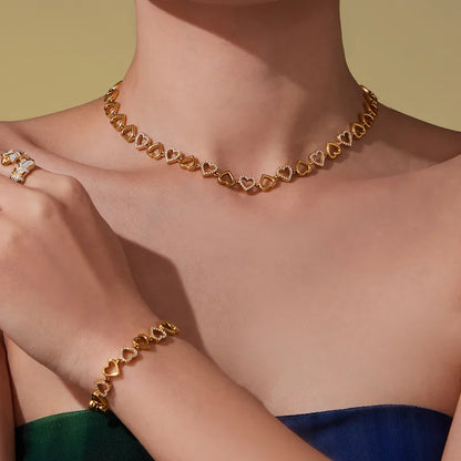 Gold heart-shaped necklace and bracelet on a person against a yellow background