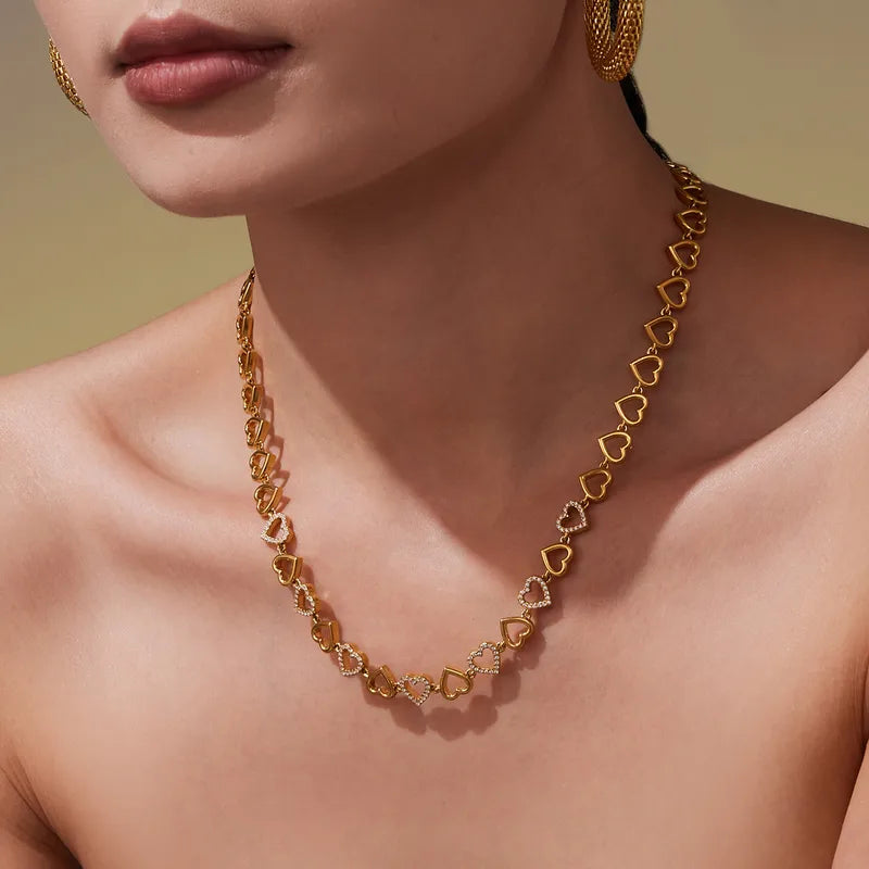 Gold necklace with heart-shaped links worn by a model against a neutral background