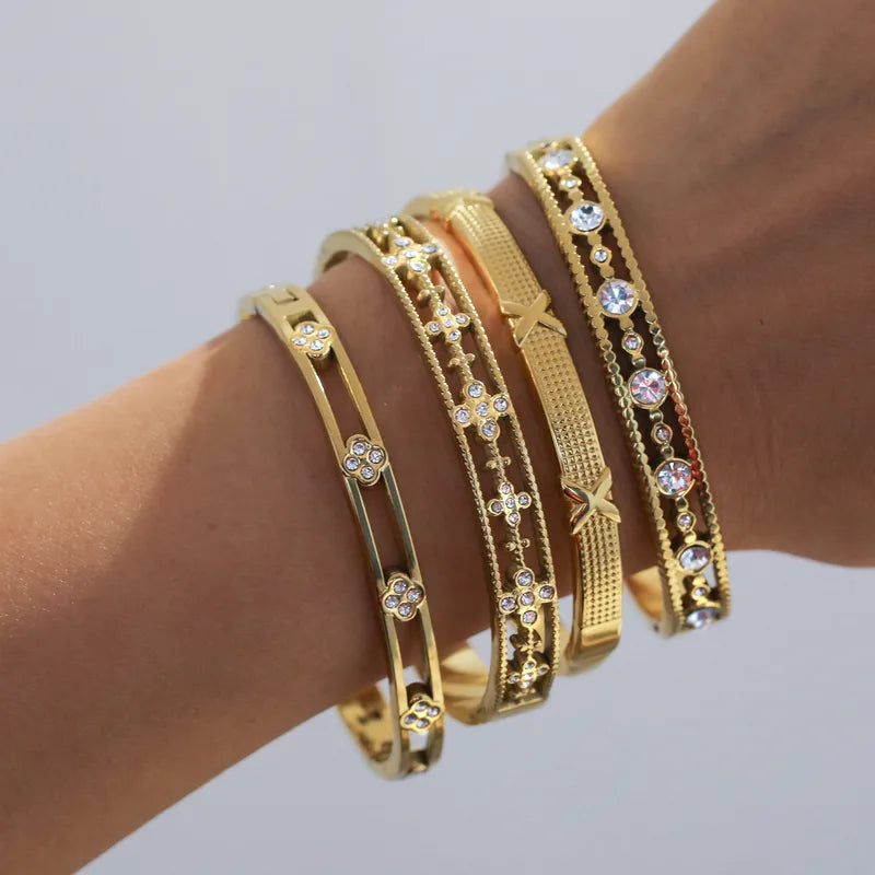 Gold bracelets with gemstones on a wrist against a light gray background