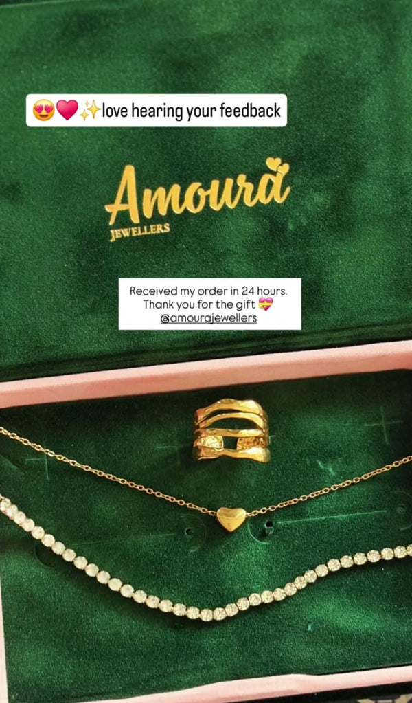 Gold jewelry set on a green cushion with 'Amoura Jewellers' branding.