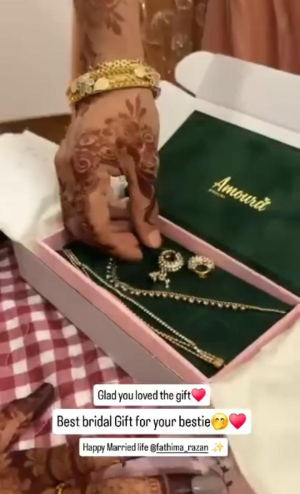 Bridal jewelry set in a 'Amoura Jewellers' box with a hand wearing gold jewelry and henna designs.
