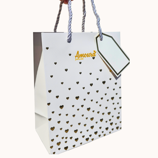 White gift bag with gold heart patterns and 'Amoura' branding on a white background