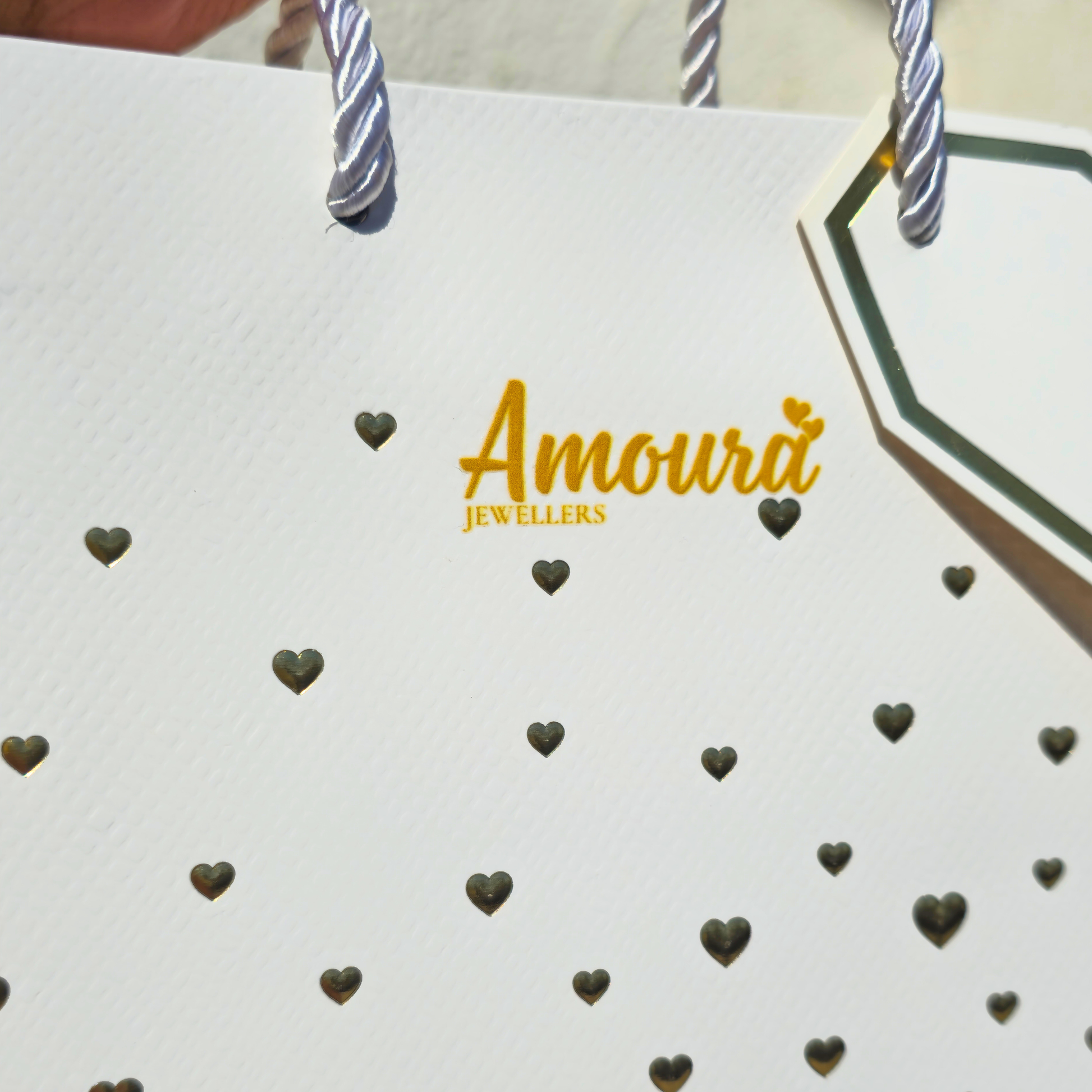 White shopping bag with 'Amoura Jewellers' branding and heart patterns.