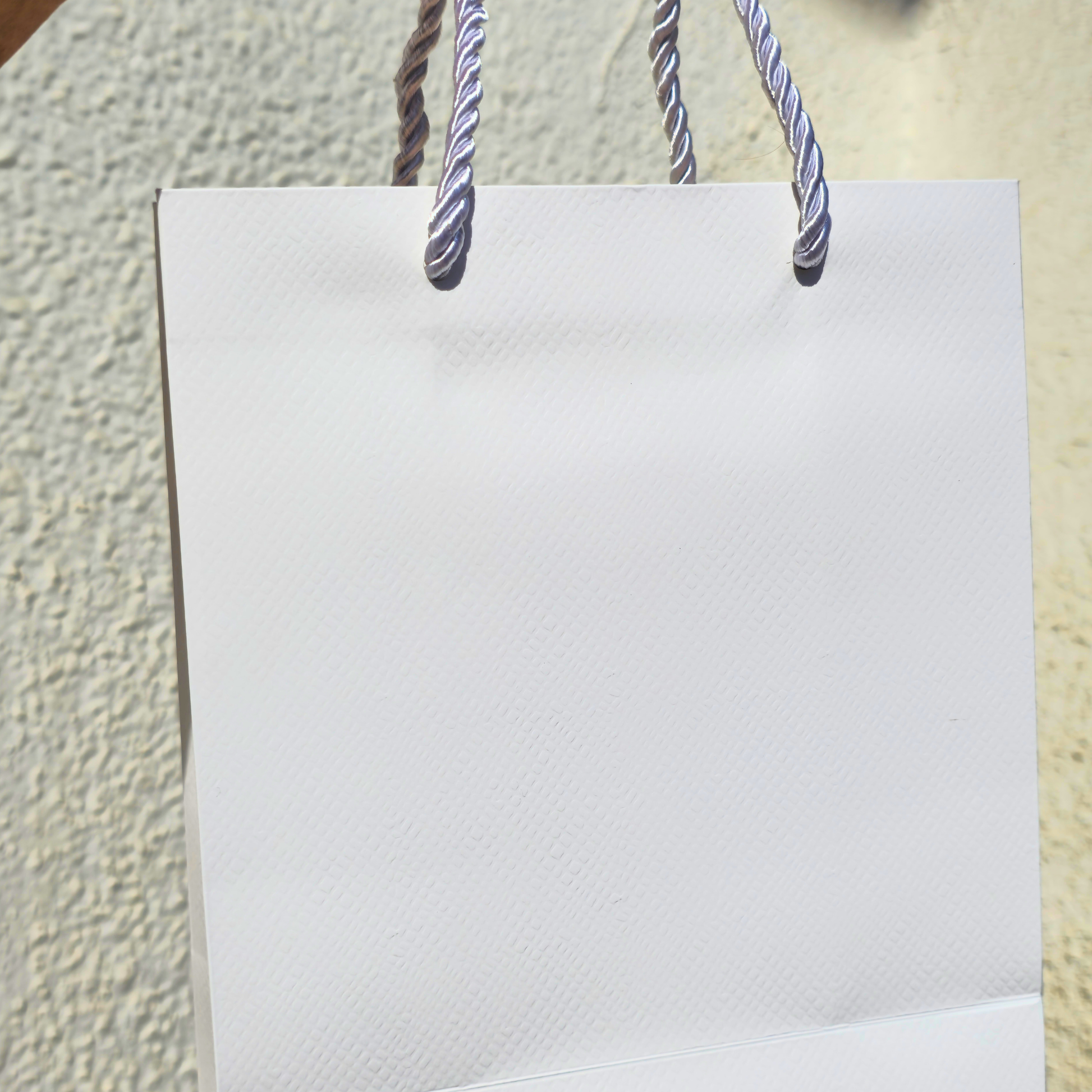 White paper bag with striped handles against a textured beige wall