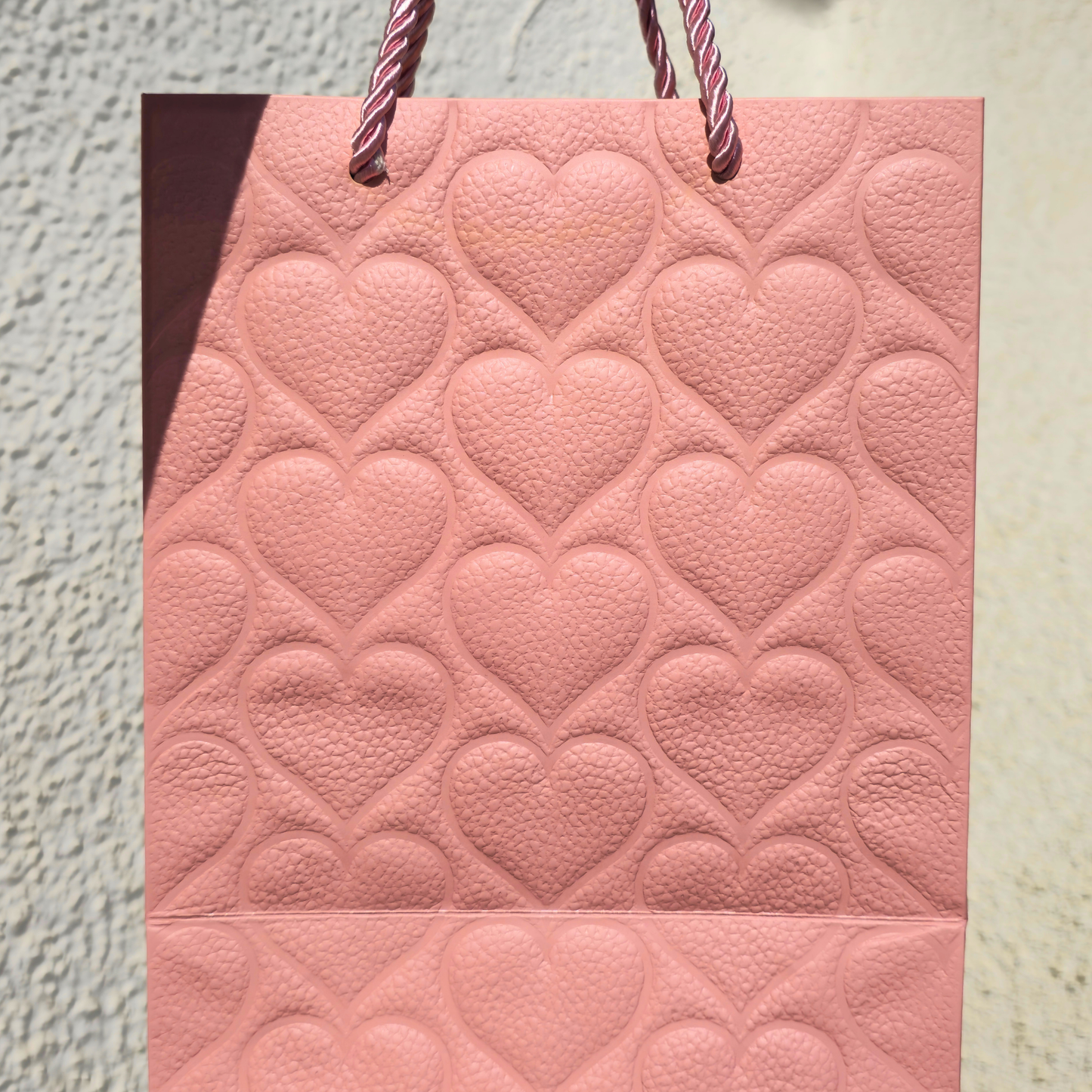 Pink gift bag with heart pattern on a textured surface