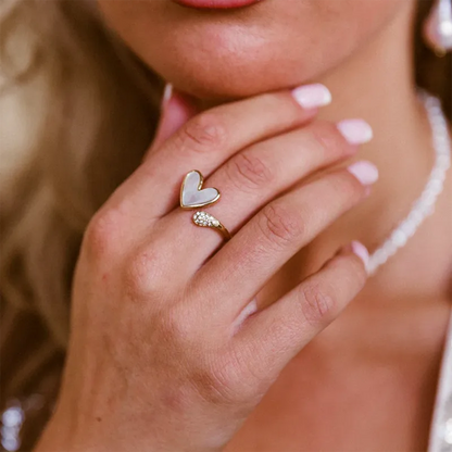 Close-up of a hand wearing a heart-shaped ring with a diamond, blurred background