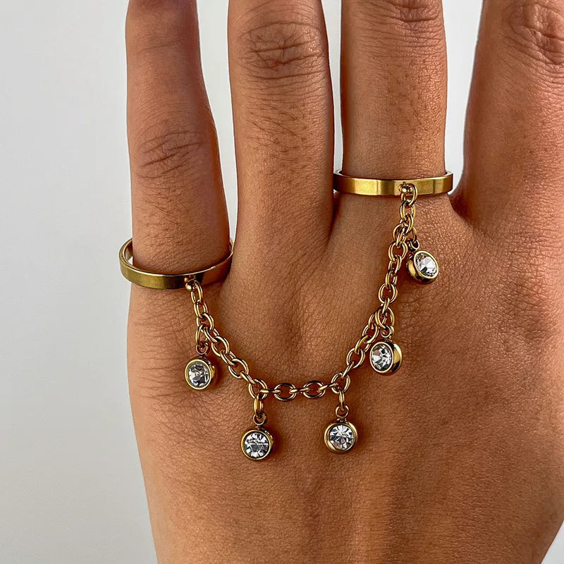 Gold ring with chain and charms on a hand against a neutral background