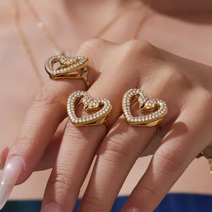 Three gold heart-shaped rings with diamond accents on a hand against a neutral background
