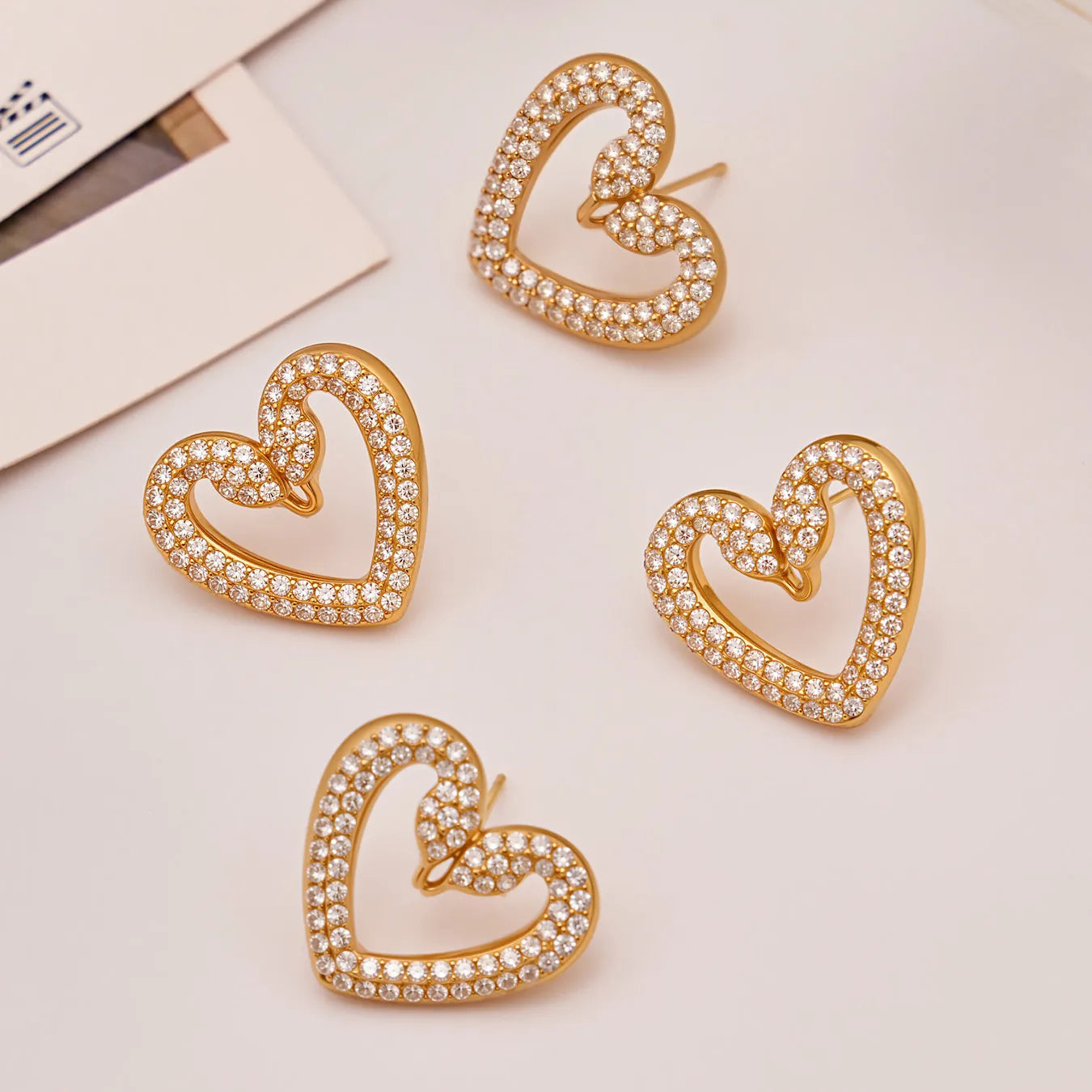 Gold heart-shaped earrings with clear stones on a light background