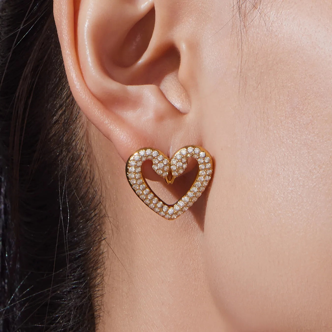 Close-up of an ear wearing a gold heart-shaped earring with pearls.