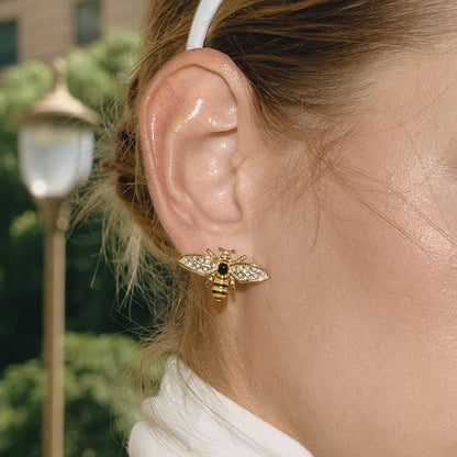 Close-up of a person wearing a gold bee-shaped earring with a black gemstone, outdoors.