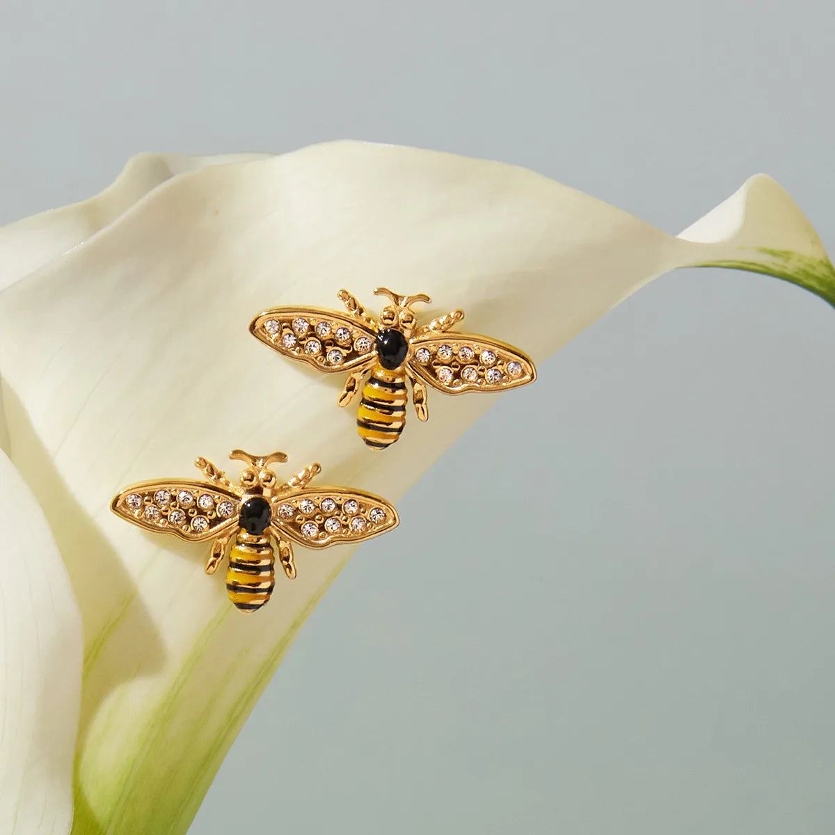 Gold bee-shaped earrings with gemstones on a white flower petal.
