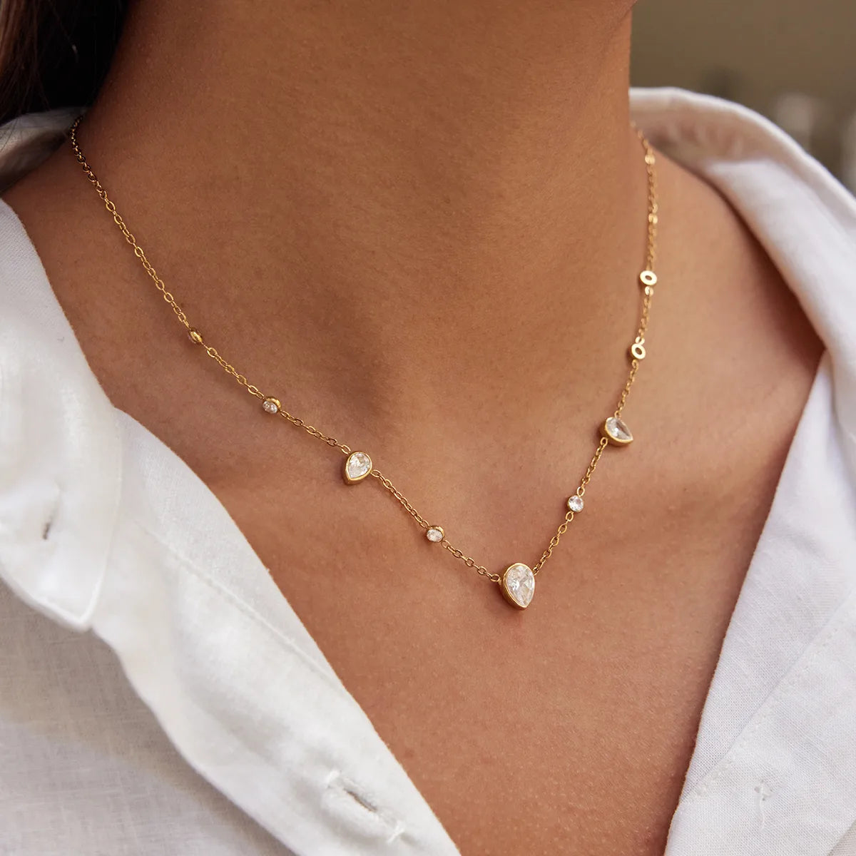 Gold necklace with teardrop-shaped pendants on a person wearing a white shirt.